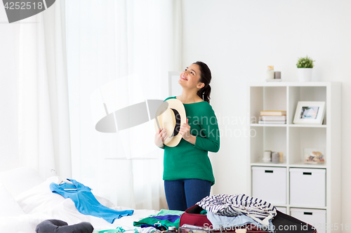Image of happy woman with hat packing travel bag at home