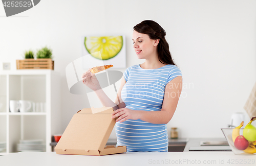 Image of happy pregnant woman eating pizza at home kitchen