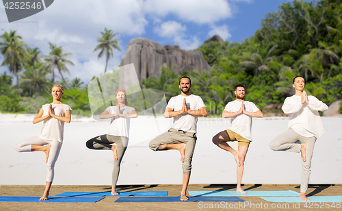 Image of people making yoga in tree pose on mats outdoors