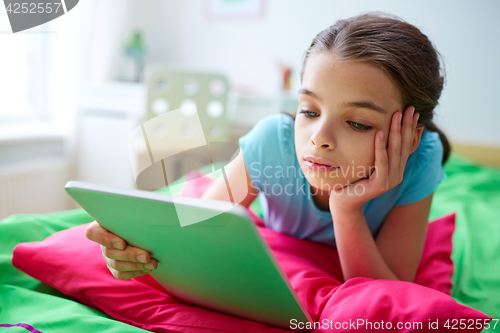 Image of smiling girl with tablet pc lying in bed at home