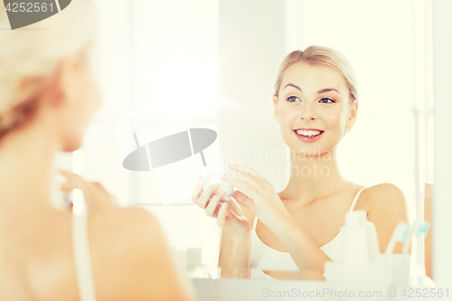 Image of happy woman applying cream to face at bathroom