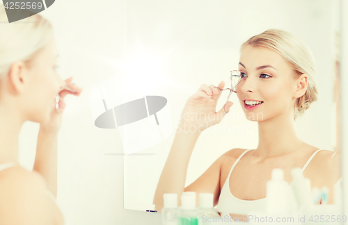 Image of woman with curler curling eyelashes at bathroom
