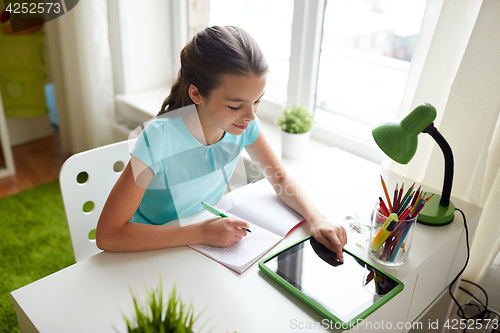 Image of girl with tablet pc writing to notebook at home