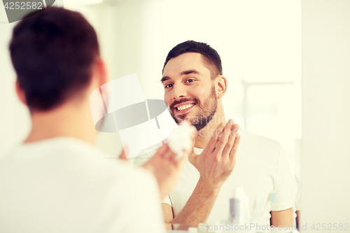 Image of happy man applying shaving foam at bathroom mirror