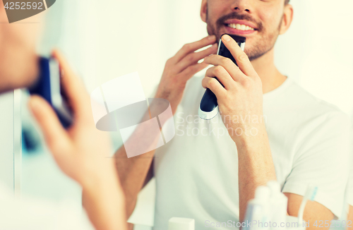 Image of close up of man shaving beard with trimmer