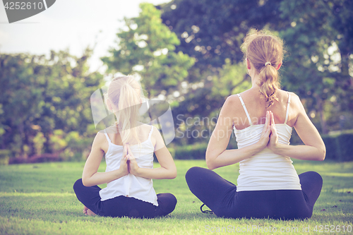 Image of Mother and daughter doing yoga exercises on grass in the park.
