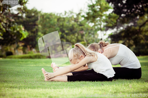 Image of Mother and daughter doing yoga exercises on grass in the park.