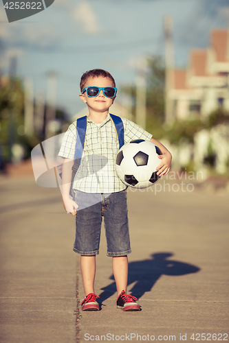 Image of Caucasian little boy standing on the road and holding his soccer