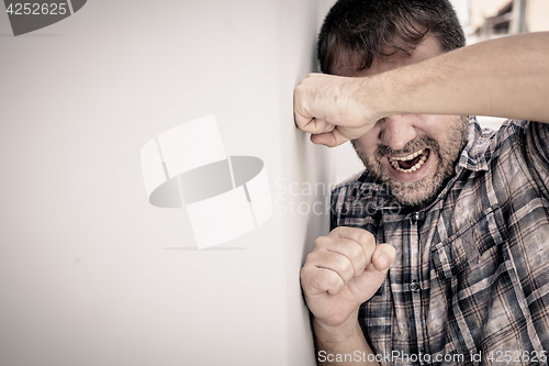 Image of portrait one sad man standing near a wall and covers his face