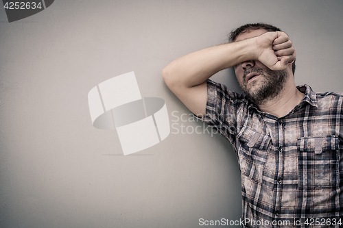 Image of portrait one sad man standing near a wall and covers his face