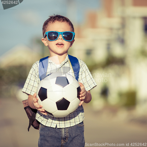 Image of Caucasian little boy standing on the road and holding his soccer