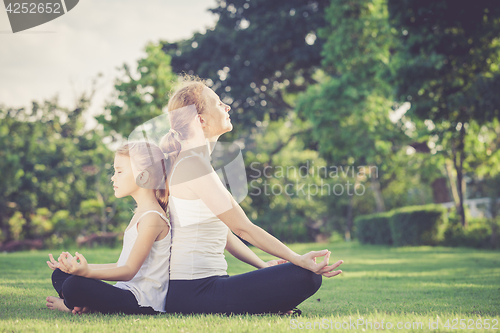 Image of Mother and daughter doing yoga exercises on grass in the park.