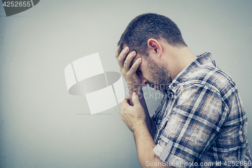 Image of portrait one sad man standing near a wall and covers his face