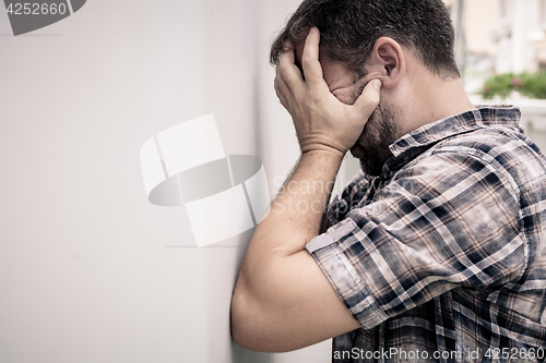 Image of portrait one sad man standing near a wall and covers his face