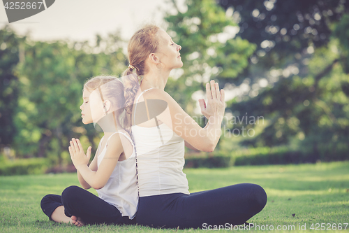 Image of Mother and daughter doing yoga exercises on grass in the park.