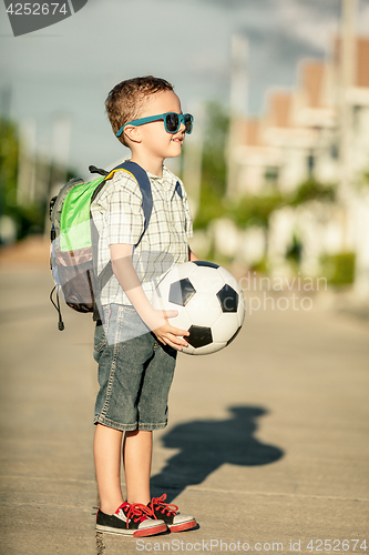 Image of Caucasian little boy standing on the road and holding his soccer