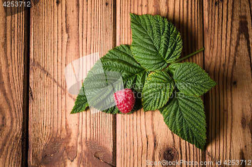 Image of Berry raspberries with leaves on a wooden surface, close-up