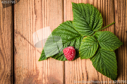 Image of Berry raspberries with leaves on a wooden surface, close-up