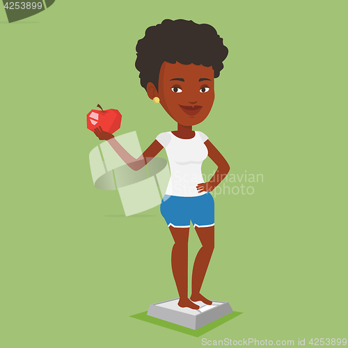 Image of Woman standing on scale and holding apple in hand.