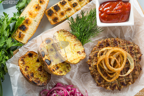 Image of burger grill with vegetables, sauce on a wooden surface. potatoes and bread