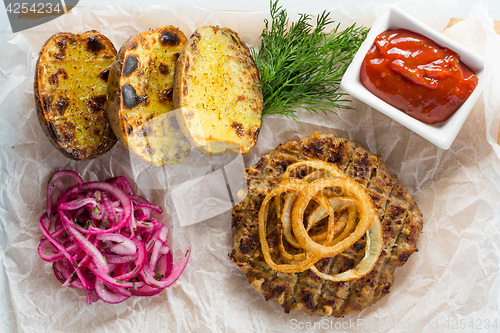 Image of burger grill with vegetables, sauce on a wooden surface. potatoes and bread
