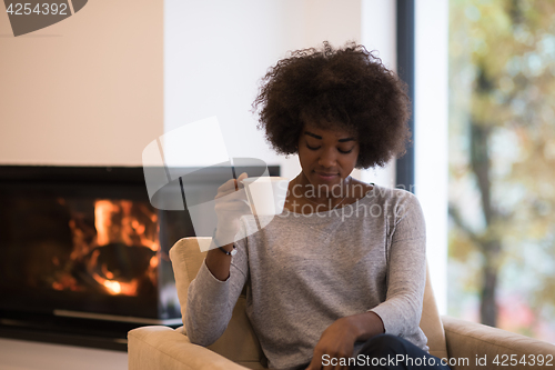 Image of black woman drinking coffee in front of fireplace