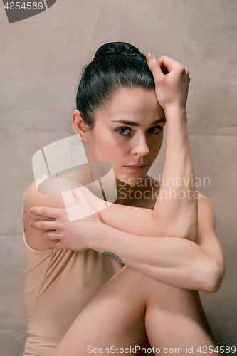 Image of Tired ballet dancer sitting on the wooden floor on a pink background