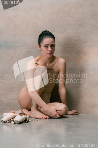 Image of Tired ballet dancer sitting on the wooden floor on a pink background