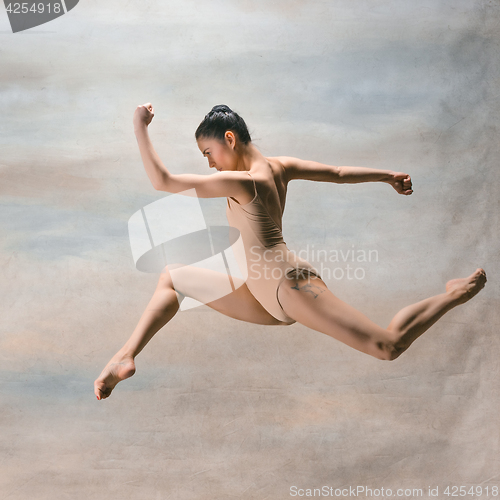 Image of Young beautiful modern style dancer jumping on a studio background