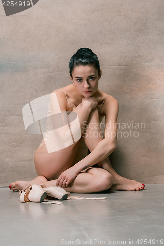 Image of Tired ballet dancer sitting on the wooden floor on a pink background