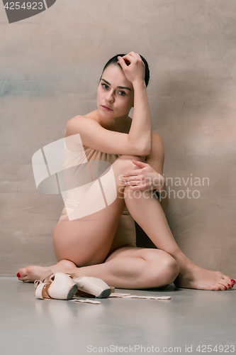 Image of Tired ballet dancer sitting on the wooden floor on a pink background