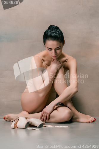 Image of Tired ballet dancer sitting on the wooden floor on a pink background