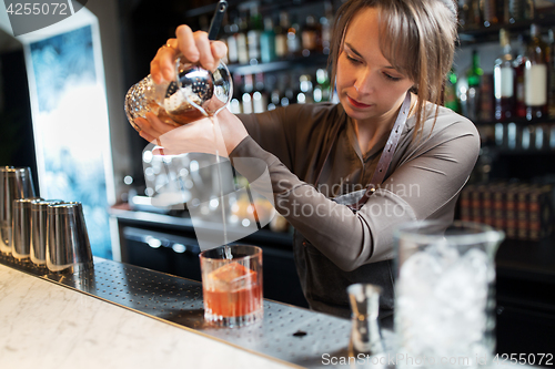 Image of barmaid with glass and jug preparing cocktail