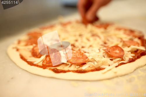 Image of cook hands adding salami to pizza at pizzeria