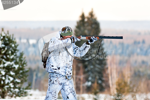 Image of the hunter in winter camouflage shooting from a gun