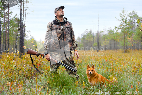 Image of hunter with a gun and a dog on the swamp