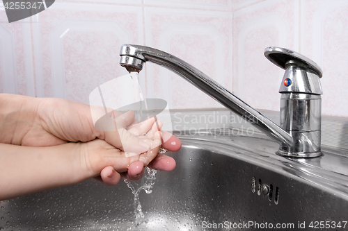 Image of A women's hand helps child to washes his hands