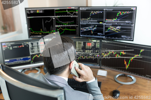 Image of Over the shoulder view of stock broker trading online, talking on mobile phone.