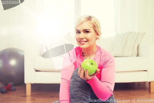 Image of happy woman eating green apple at home