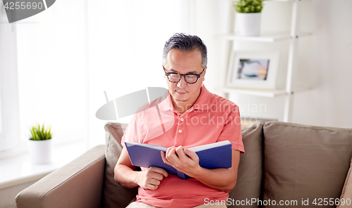 Image of man sitting on sofa and reading book at home