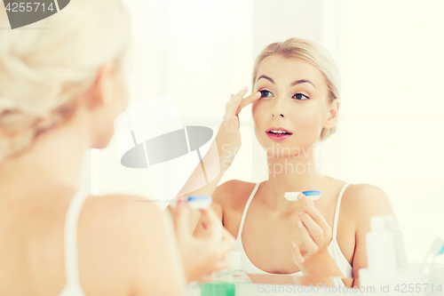 Image of young woman putting on contact lenses at bathroom