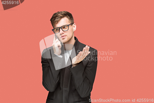 Image of The young caucasian businessman on red background talking on cell phone