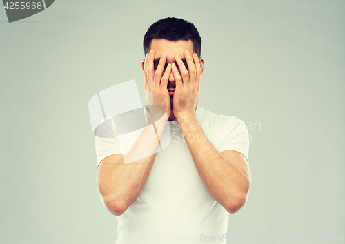 Image of man in white t-shirt covering his face with hands