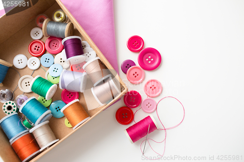 Image of box with thread spools and sewing buttons on table