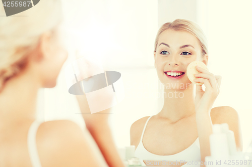 Image of young woman washing face with sponge at bathroom