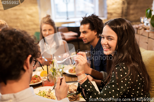 Image of happy friends eating and drinking at restaurant