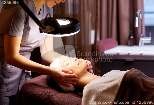 Image of beautician doing face massage to woman at spa