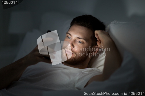 Image of young man with smartphone in bed at night