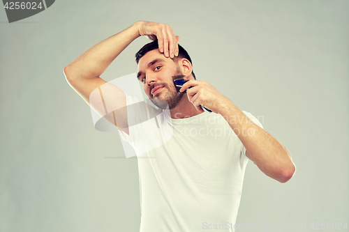 Image of smiling man shaving beard with trimmer over gray