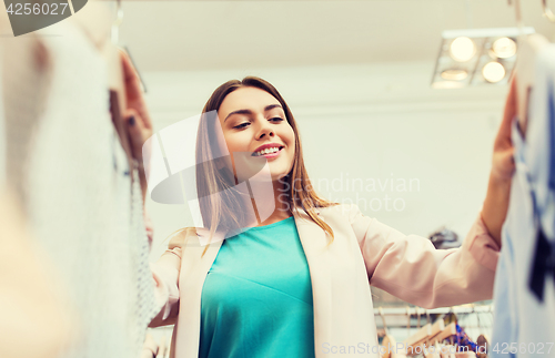 Image of happy young woman choosing clothes in mall